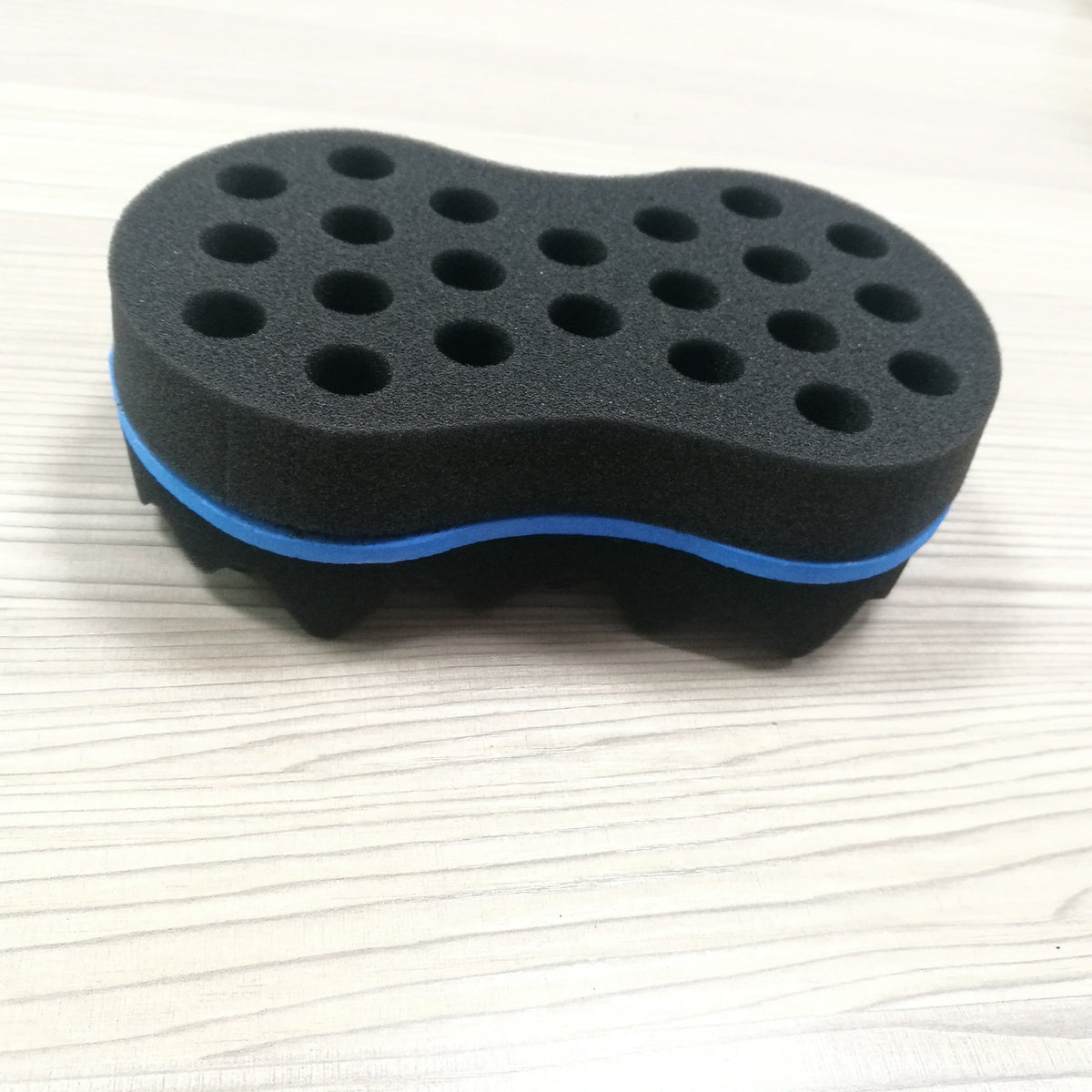 Black sponge hair twist brush with a blue stripe on a pale wooden surface